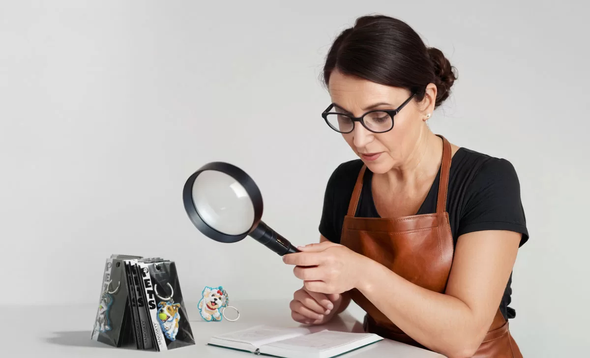 kobieta w rzemieślniczym skórzanym fartuchu sprawdzająca jakość wyrobów z pomocą lupy